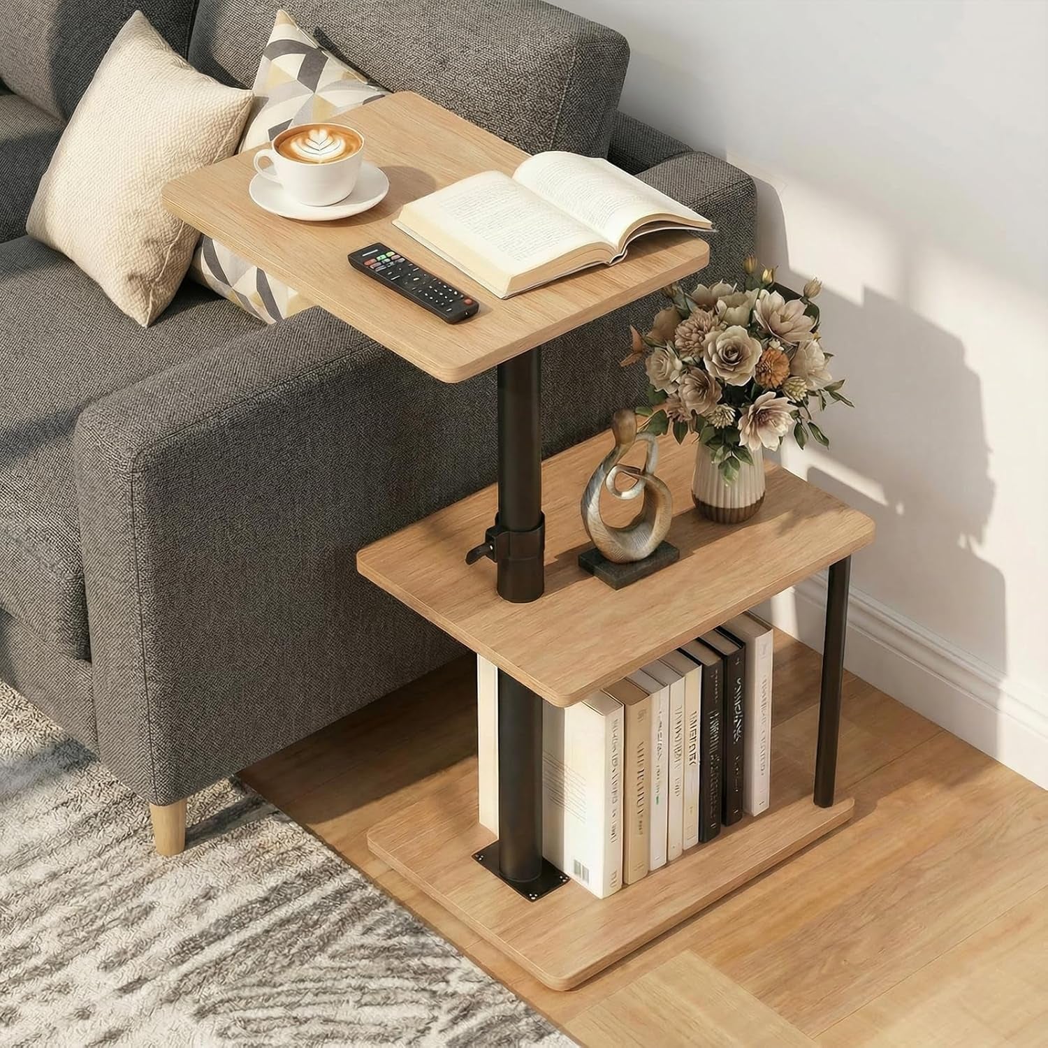 Three-tier C-shaped side table in light rustic brown beside a gray sofa with books and a vase.