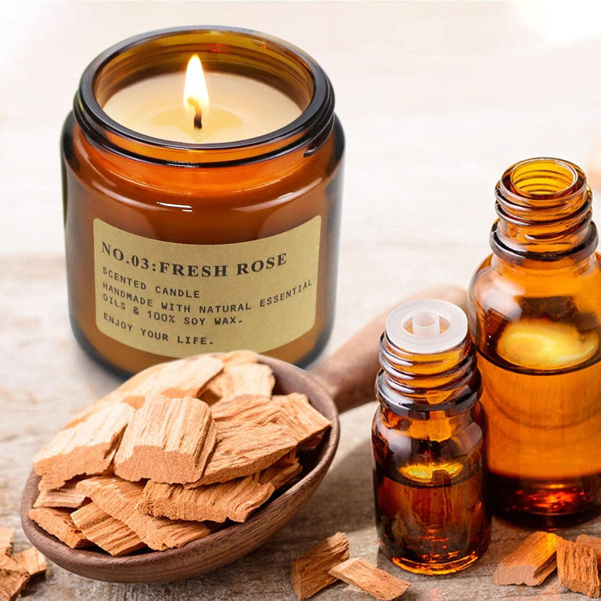 Single lit amber jar candle labeled 'Fresh Rose' beside amber essential oil bottles and wood chips