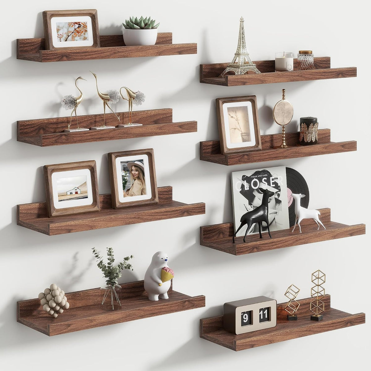 Staggered dark brown wood picture ledges on a white wall holding framed photos, sculptures and decor.