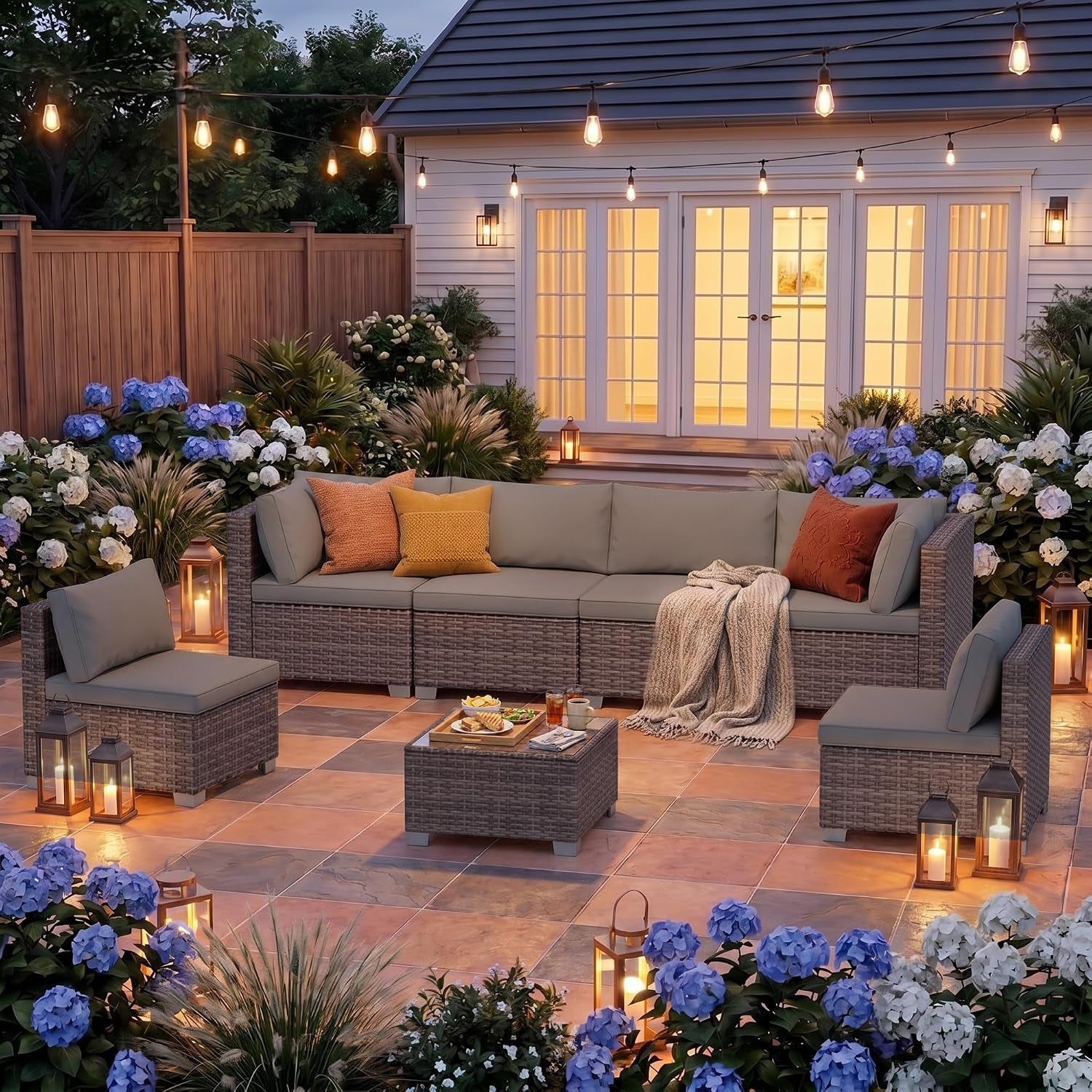 Outdoor patio setting at dusk with the rattan sectional set, coffee table, pillows and lanterns.