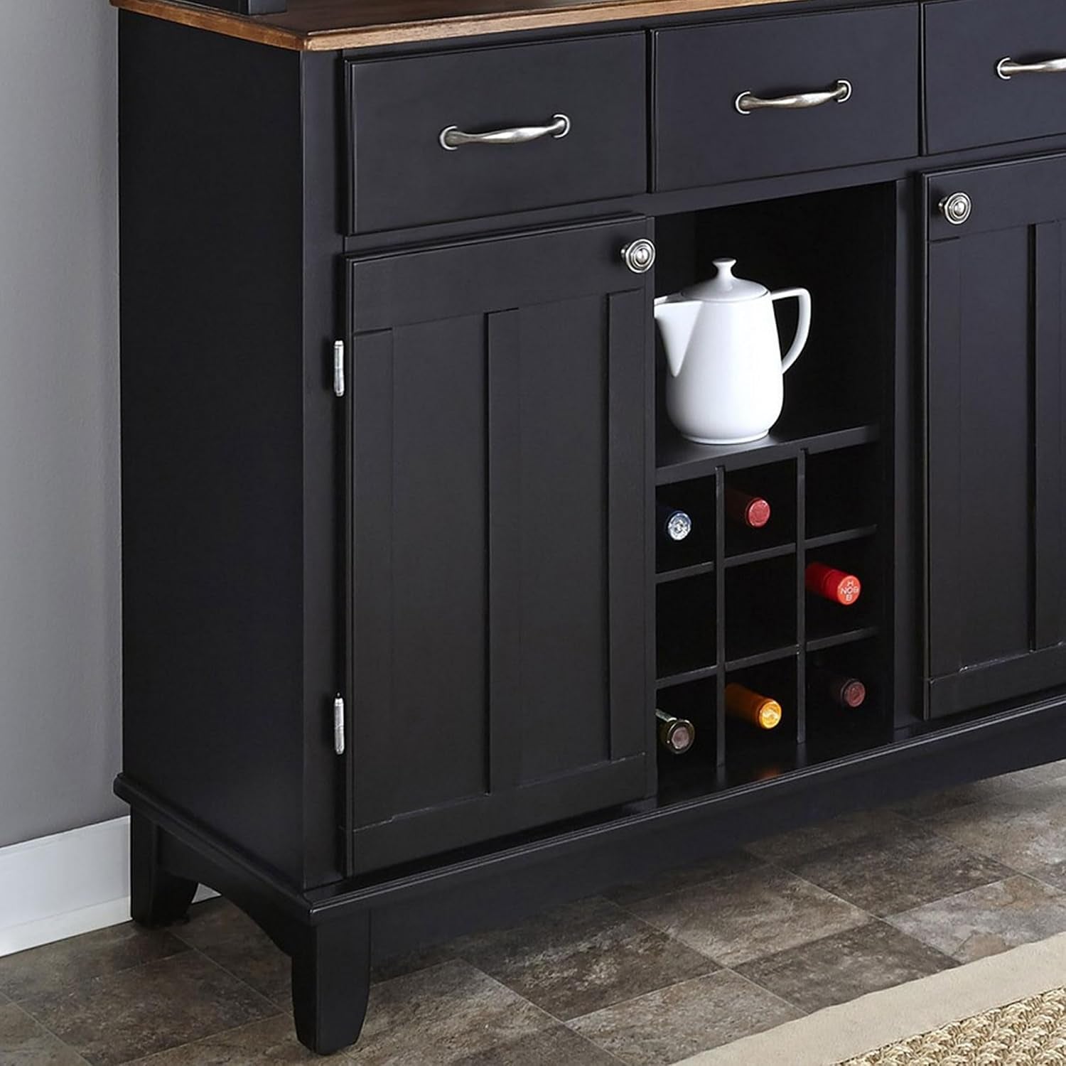 Close-up of black lower cabinet showing paneled door, wine cubby with bottles, and wood top edge.