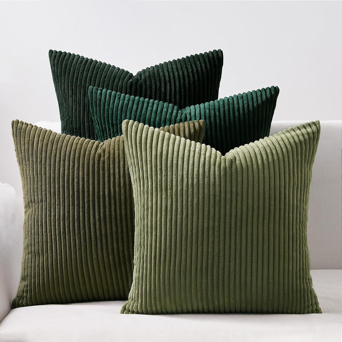 Five ribbed corduroy pillows in varying deep and muted green tones displayed on a light sofa.