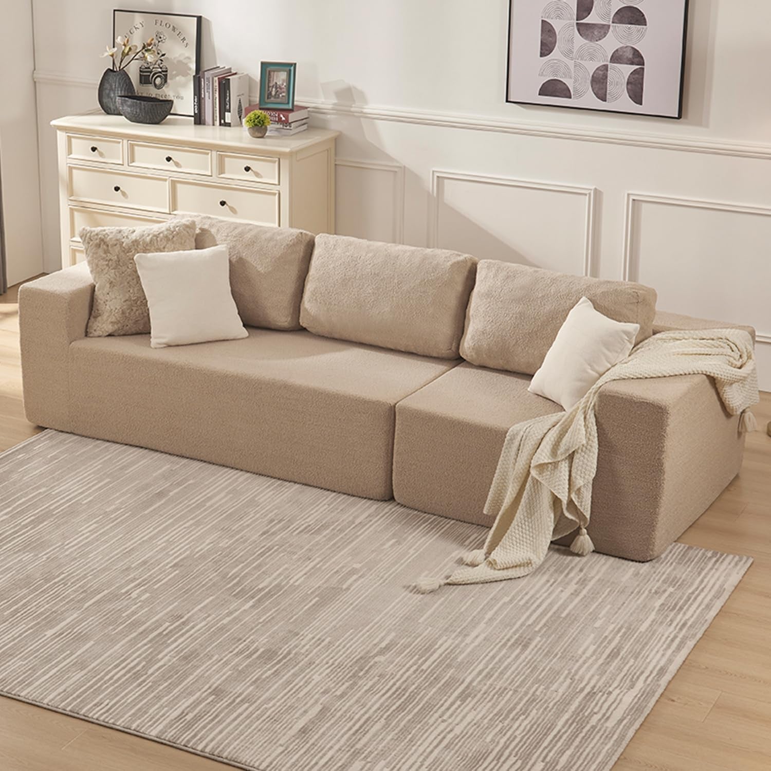 Beige low-profile modular sofa with three back cushions, throw and pillows in a styled living room.