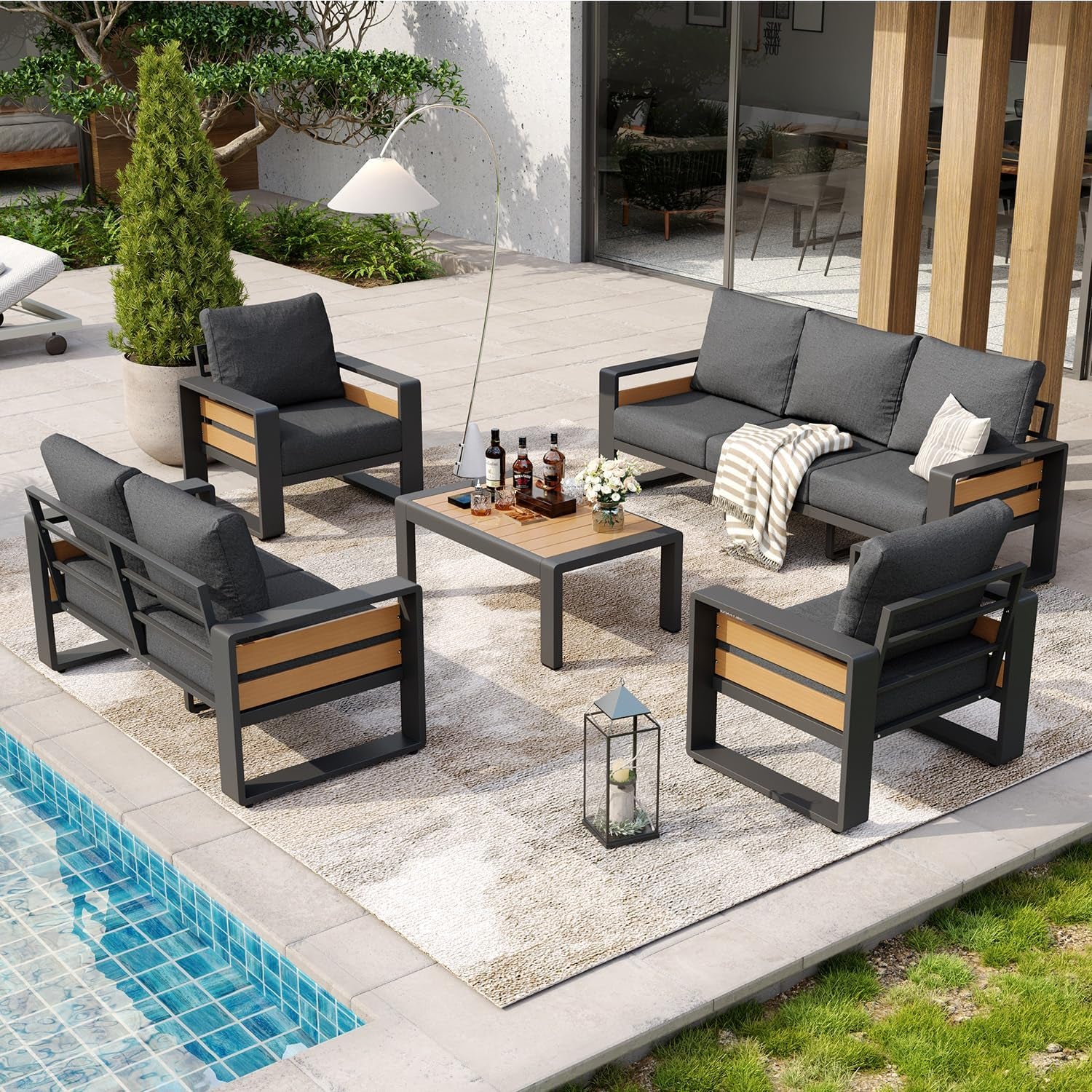 Outdoor patio sectional set with sofa, two armchairs, loveseat, and coffee table arranged on a rug beside a pool.