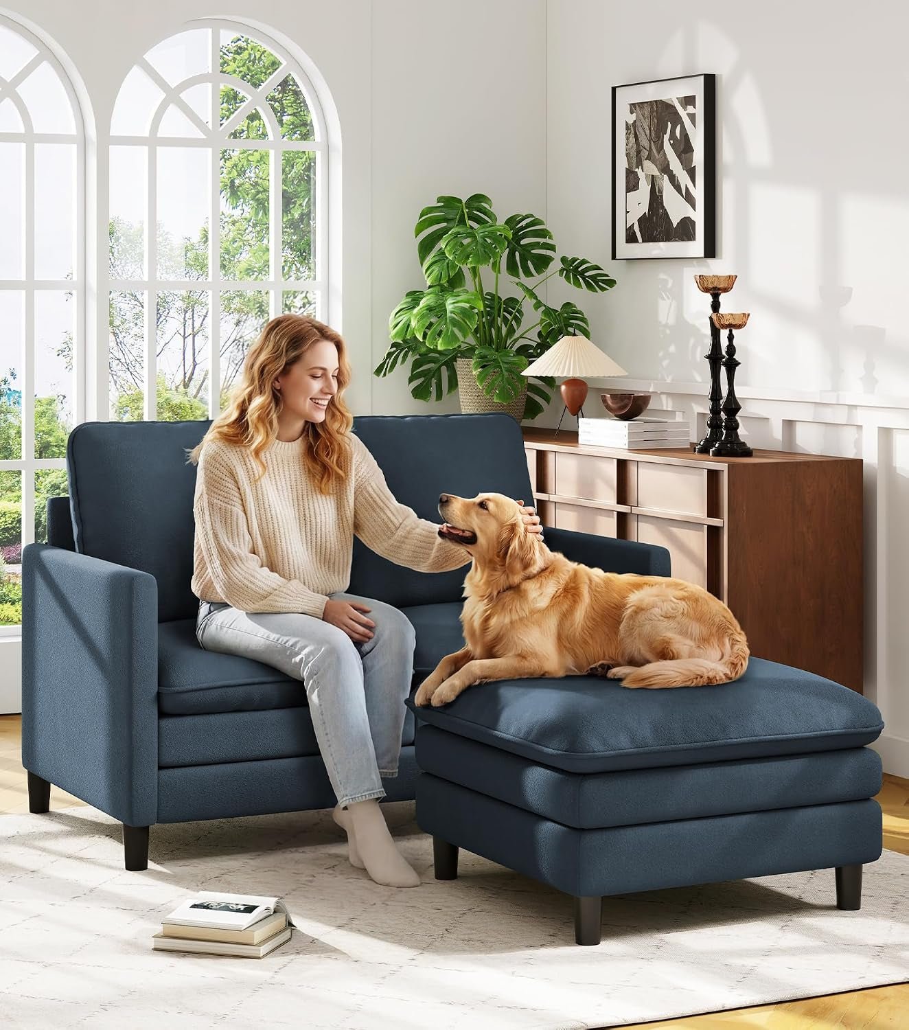 Blue loveseat and matching ottoman in a bright room with a woman petting a dog on the ottoman.