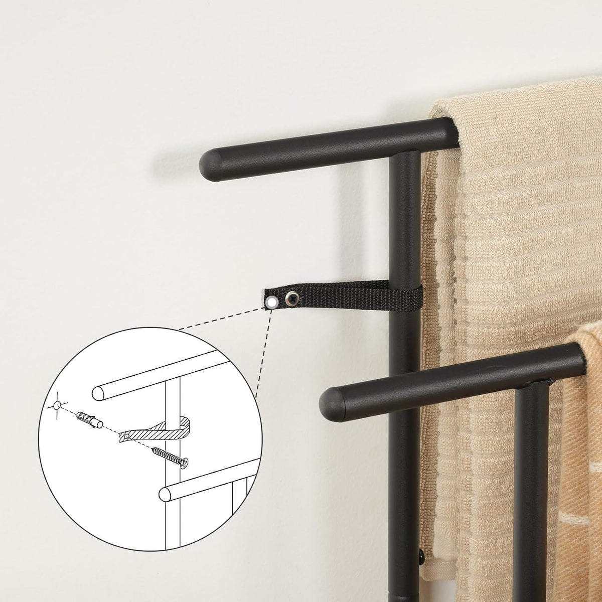 Detail of a black fabric anti-tip strap fastened to the frame with a zoomed inset diagram of a wall anchor and screw.