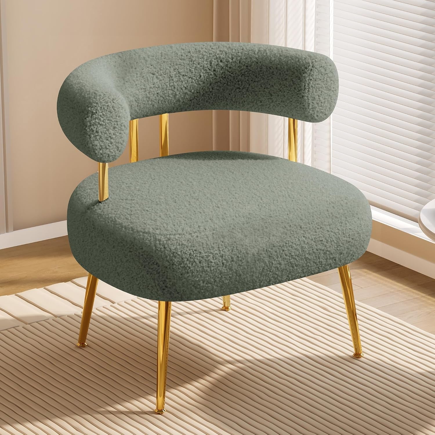 Sage green sherpa barrel chair with shiny gold legs on a striped rug by sunlit blinds.