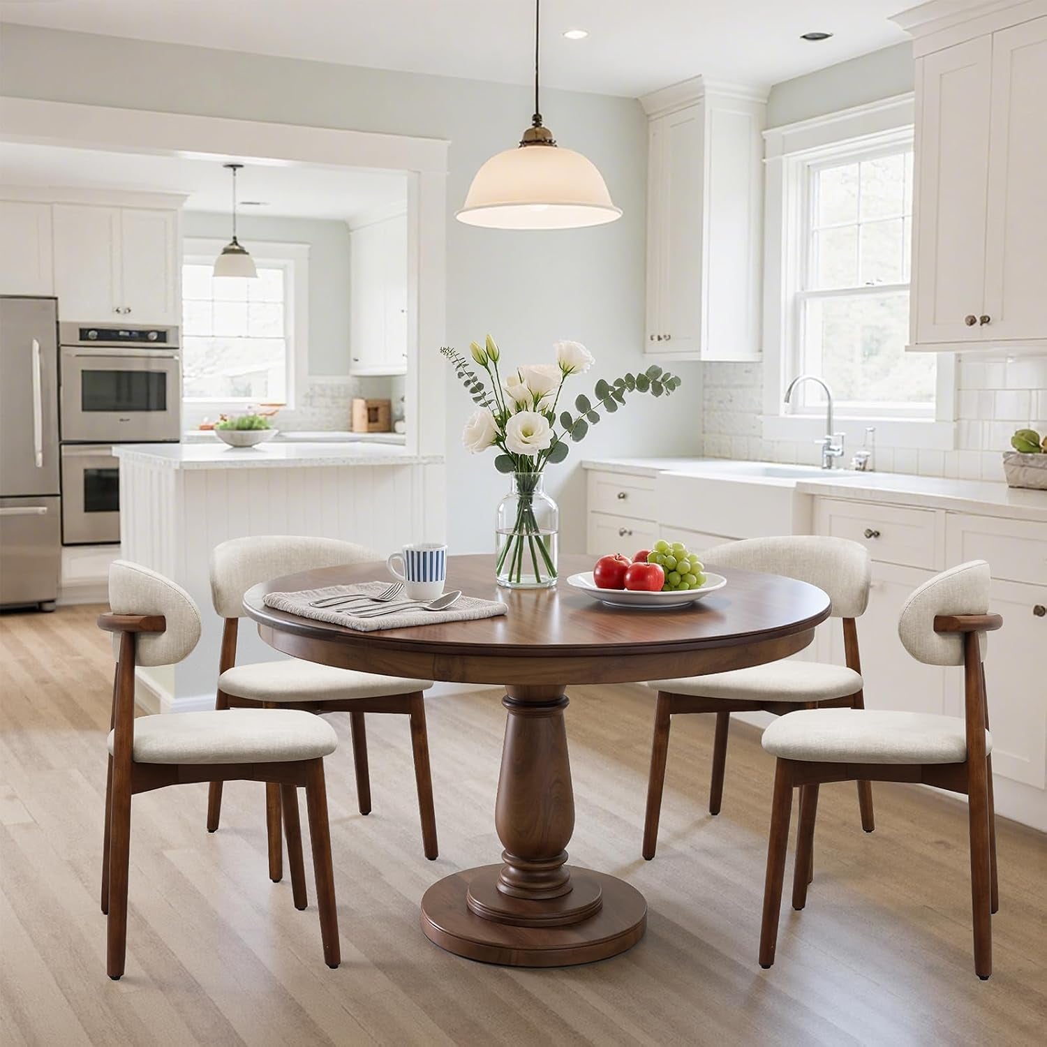 Four cream curved-back dining chairs surround a round table in a bright white kitchen.