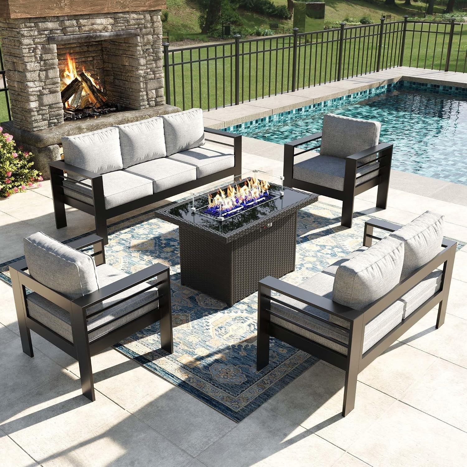 Overhead view of a four-piece seating set arranged around a woven fire pit table on a poolside patio rug.