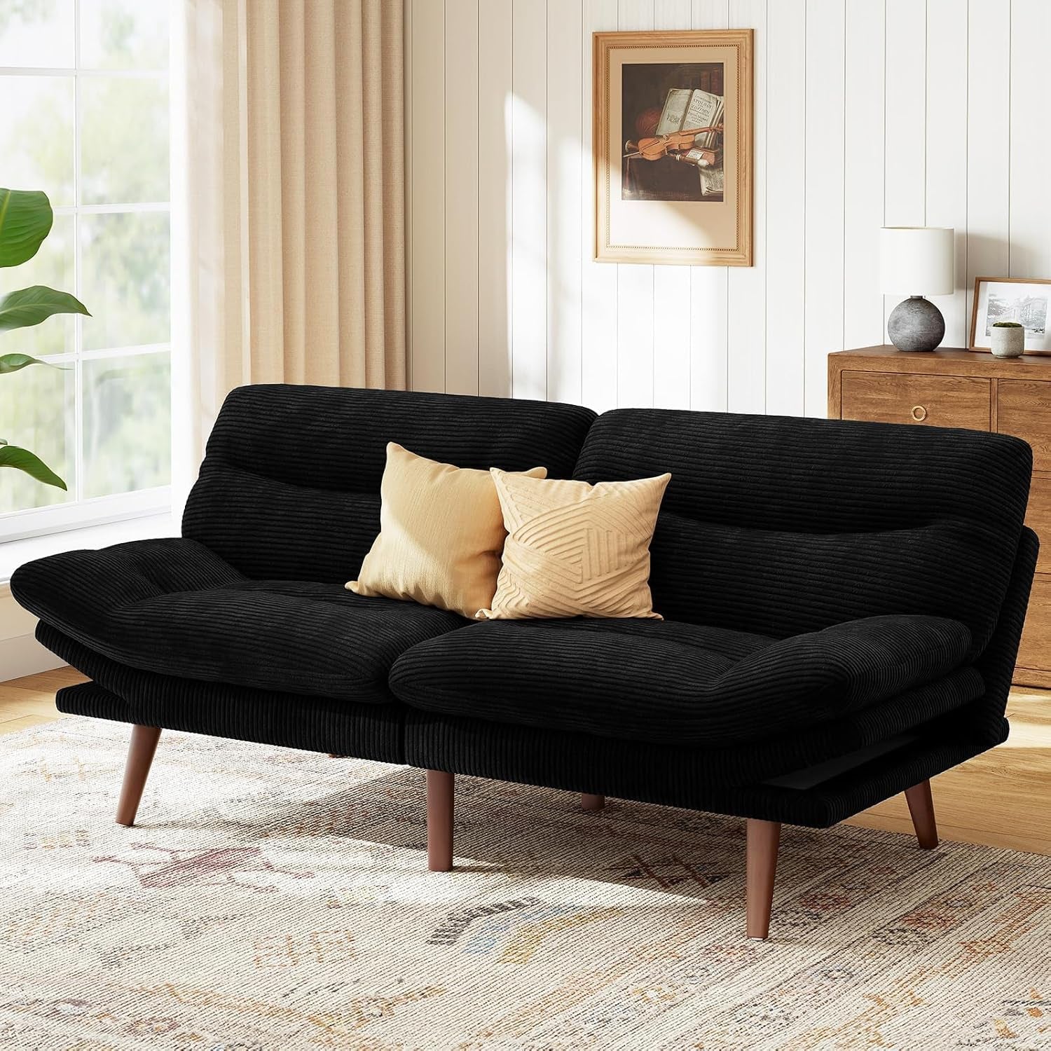 Black corduroy futon sofa with two beige pillows in a sunlit living room.