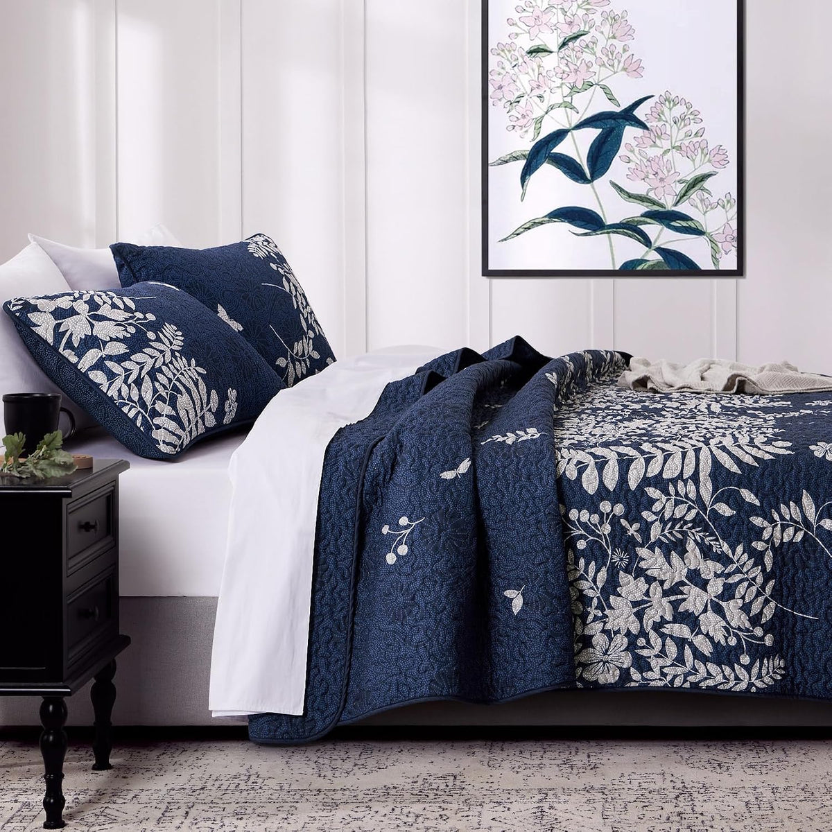 Close side view of navy quilt draped over mattress showing floral print, piping and folded edge