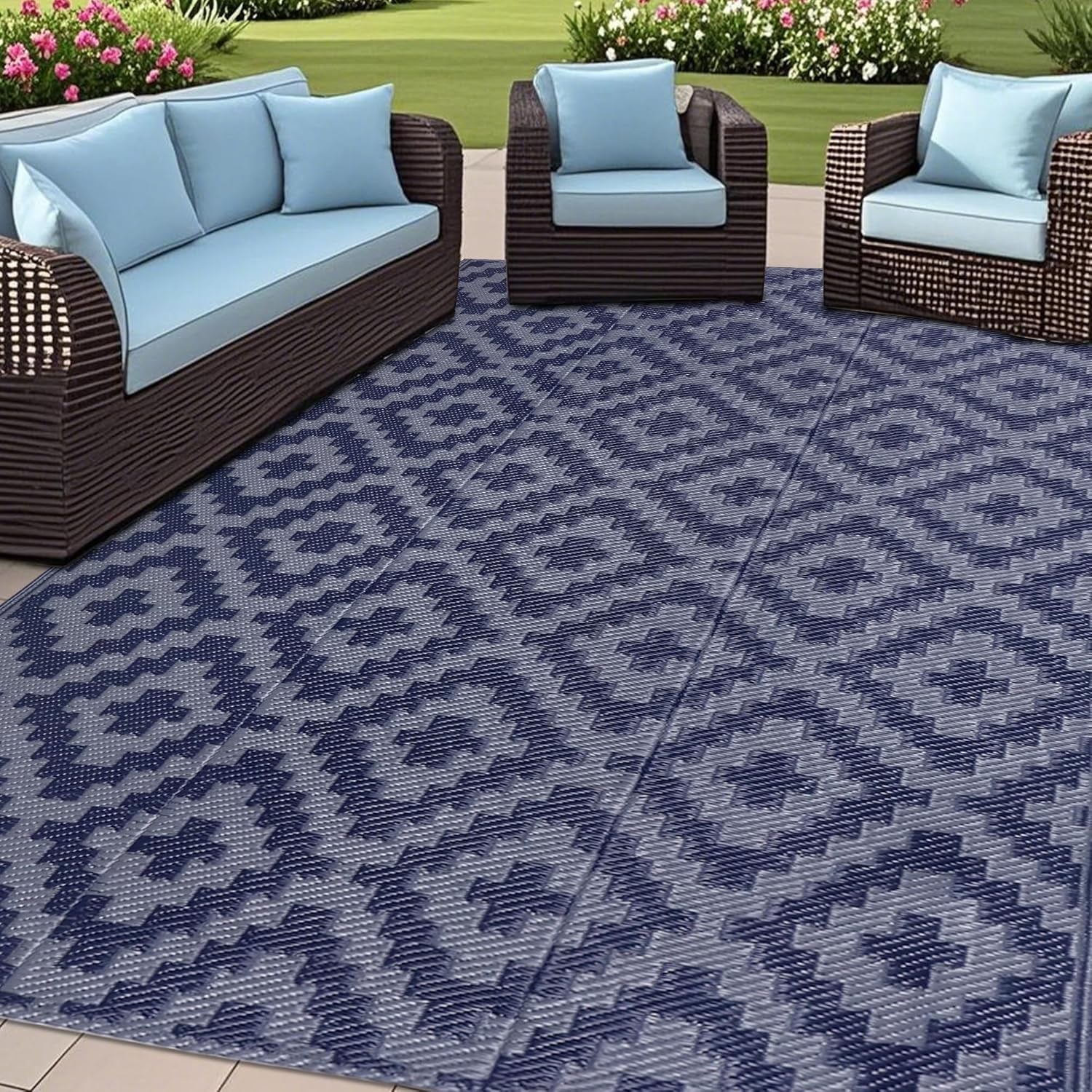 Patio furniture on a blue-gray patterned outdoor rug with a lawn and flowers behind.
