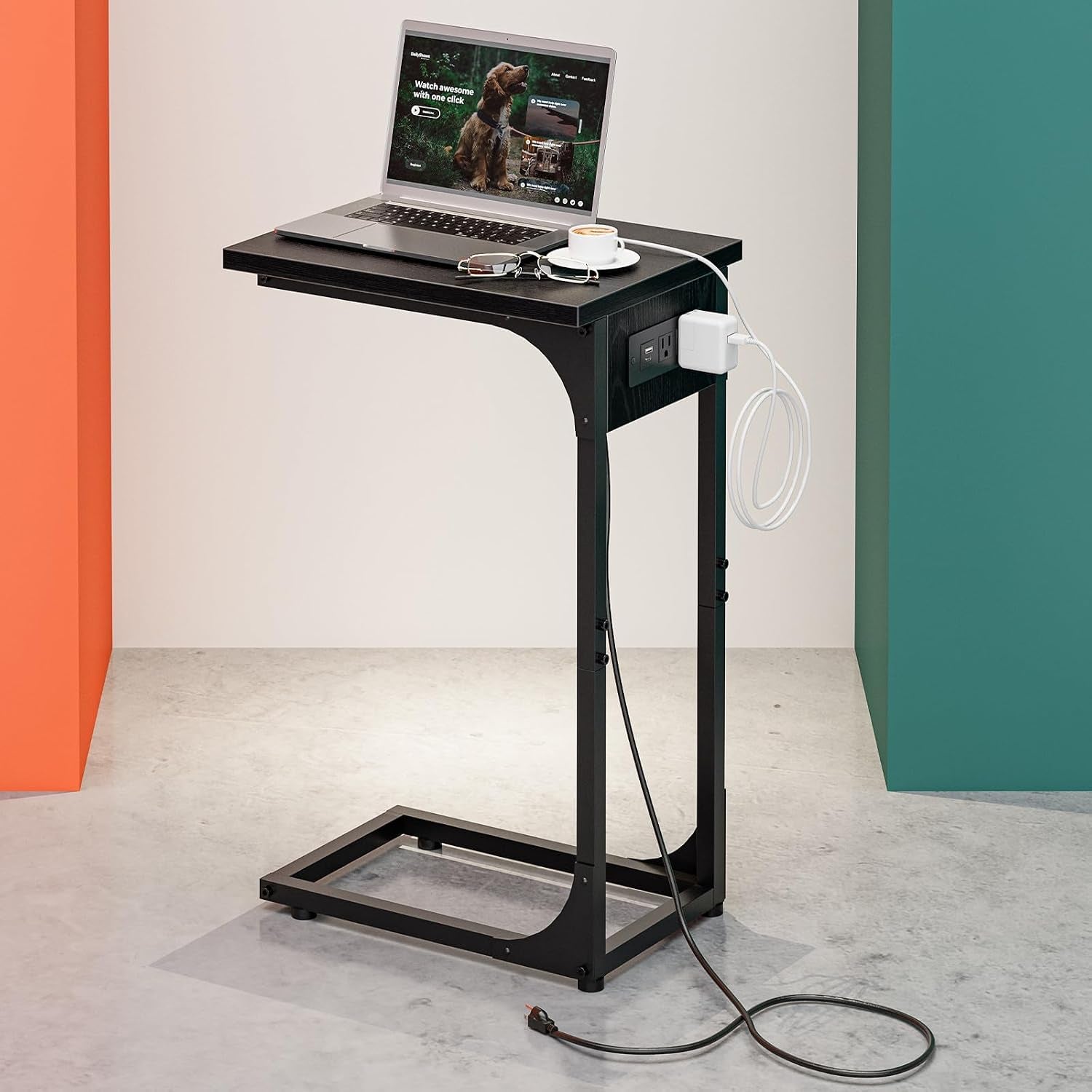 Black C-shaped side table with waterproof black top, laptop and charger plugged into side outlet.