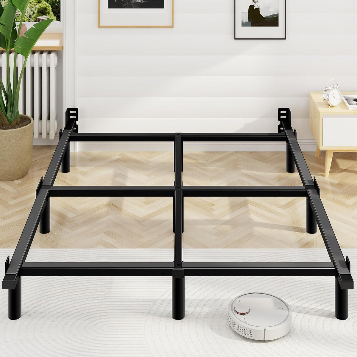 Black steel adjustable bed frame front angled view showing support legs and a robot vacuum nearby