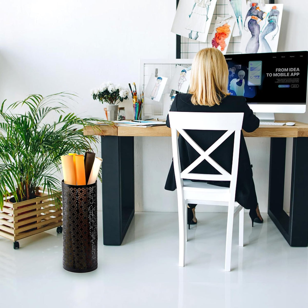 Umbrella stand next to a desk and plant in a bright home office, filled with rolled posters and papers.