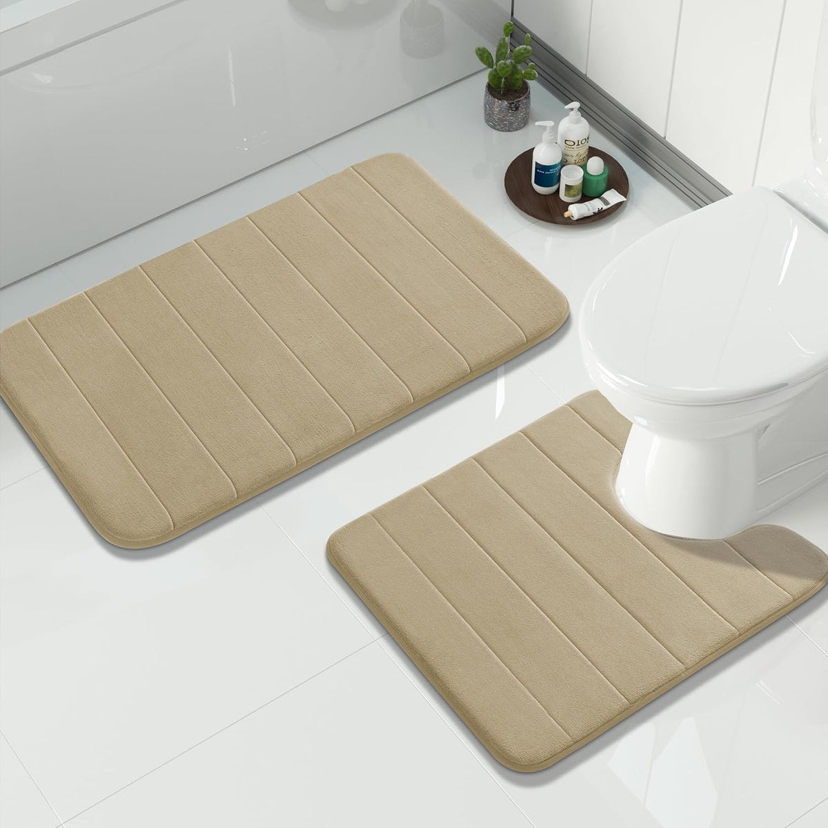 Beige two-piece bath rug set on white tile beside a toilet and bathtub, rectangular and contour mats visible
