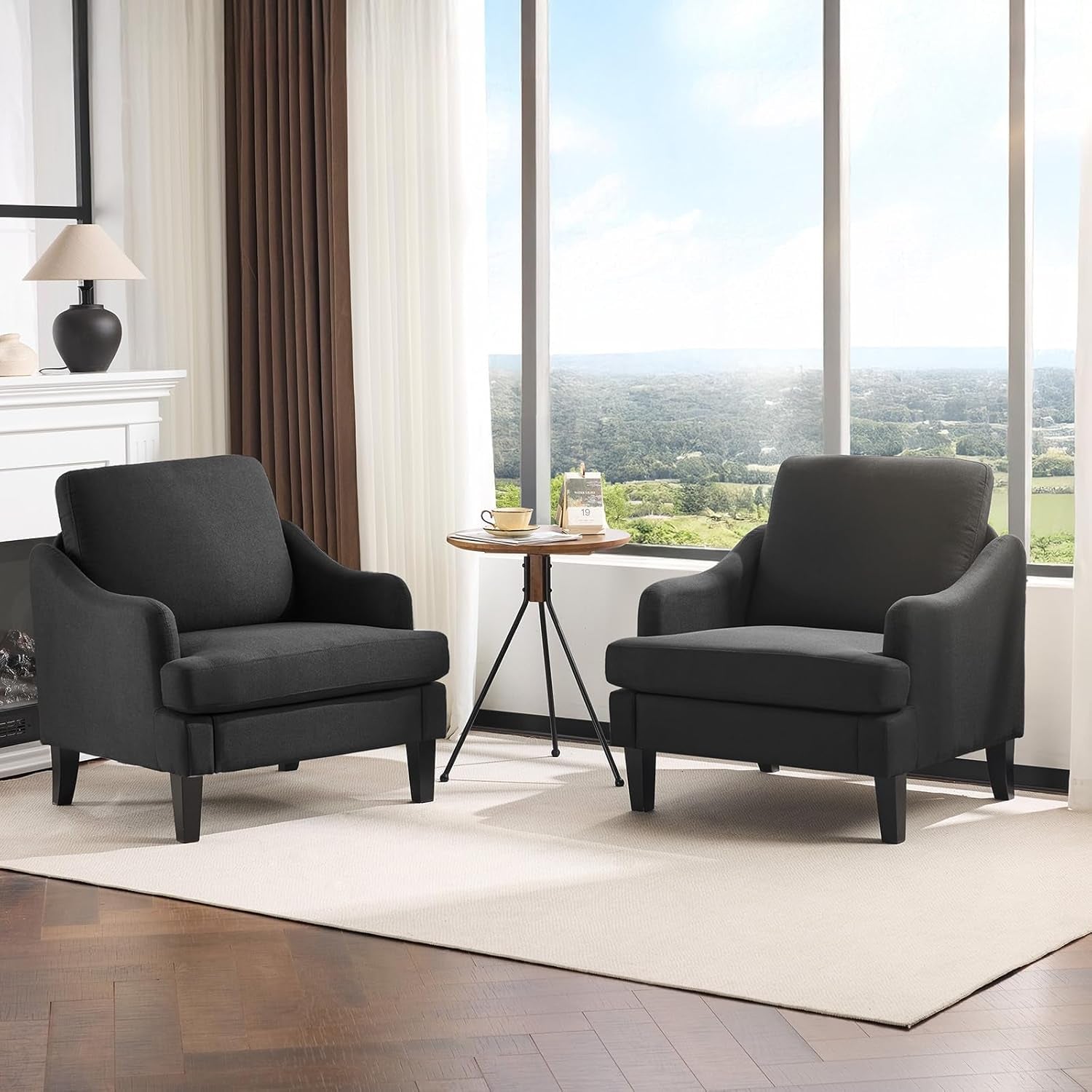 Pair of charcoal-gray upholstered armchairs flanking a small tripod side table in front of large windows.
