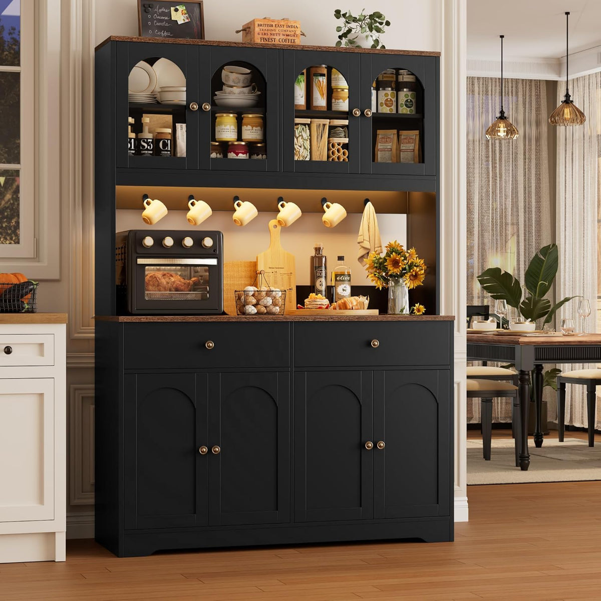 Black tall pantry showing countertop workspace, hanging mugs, toaster oven and a vase of sunflowers.