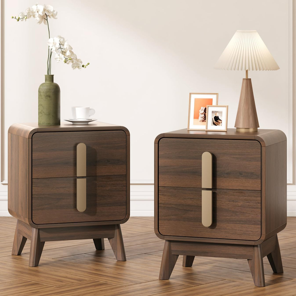 Pair of dark walnut nightstands on splayed legs with long gold pulls, styled with an orchid in a green vase, lamp and framed
