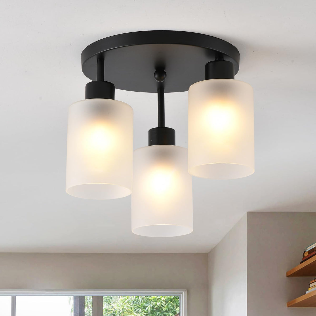 Close angled view of a three-light matte black ceiling fixture with frosted cylindrical glass shades lit