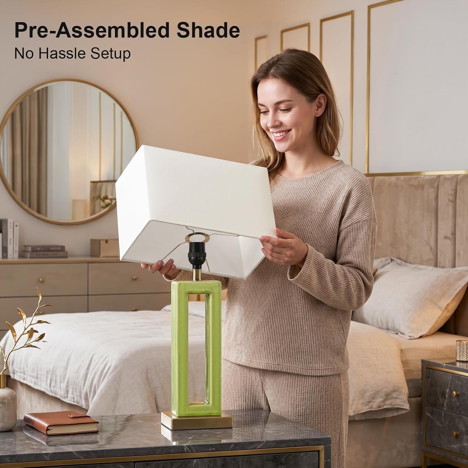Person placing a pre-assembled beige rectangular shade onto a green ceramic hollow rectangular lamp base in a bedroom
