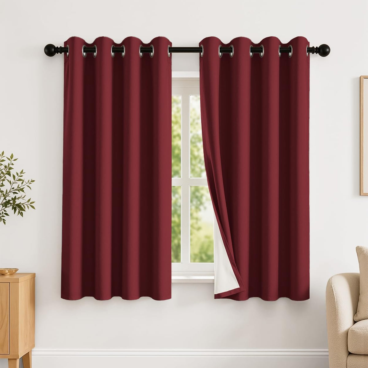 Burgundy grommet-top curtains with one panel pulled aside to expose white blackout backing at a window.