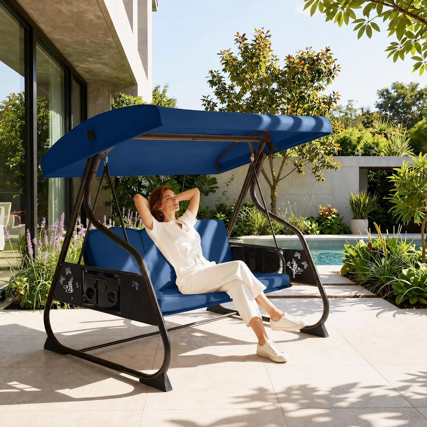 Woman reclining on a blue-canopy porch swing beside a pool and garden.
