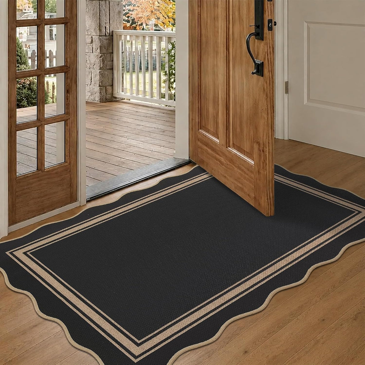 Open front door revealing a scalloped black rug with tan double-border on wood floor