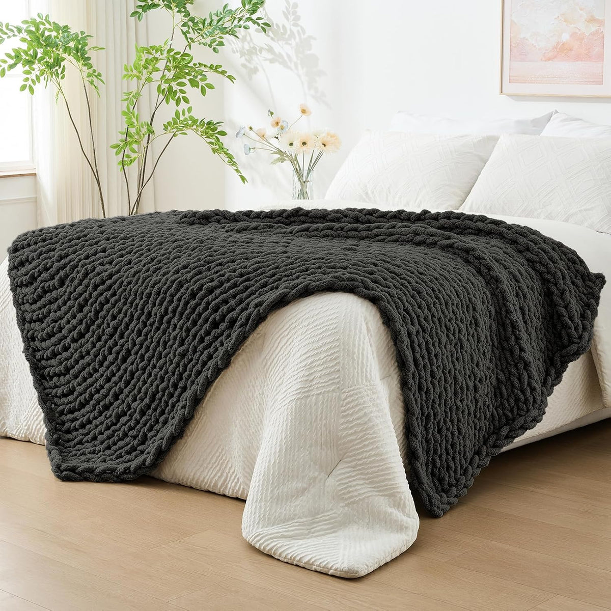 Dark charcoal chunky knit throw draped across the foot of a bed in a bright bedroom