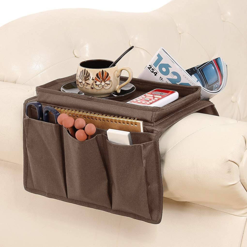 Brown fabric armrest caddy draped over a cream sofa arm holding a mug, notebook and remote