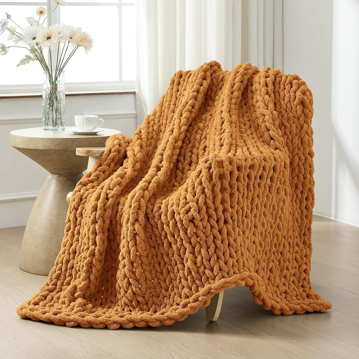 Warm burnt-orange chunky knit throw casually draped over a lounge chair beside a small round table