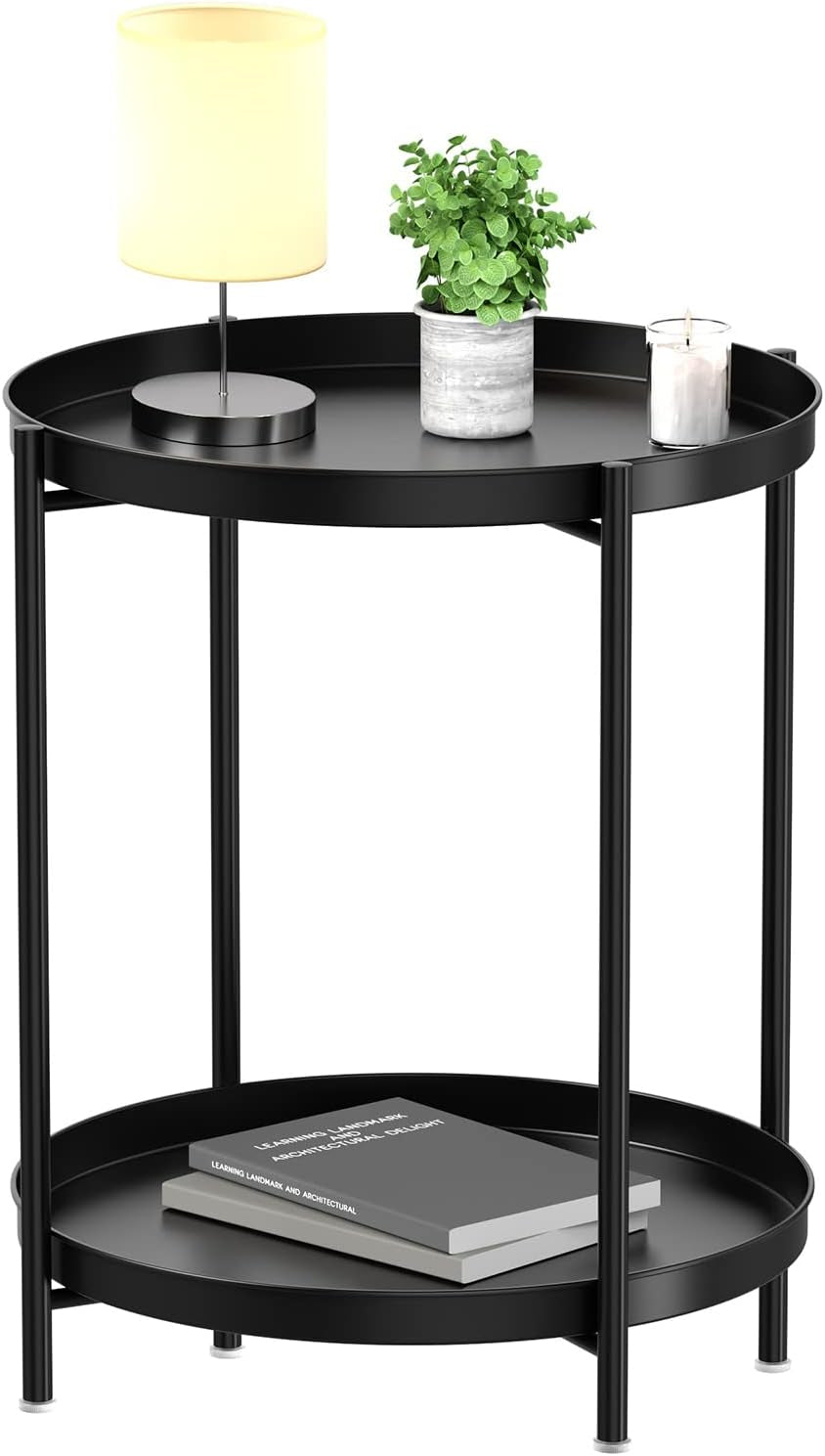 Round black two-tier metal side table with raised edges, lamp and plant on top, books on lower shelf.