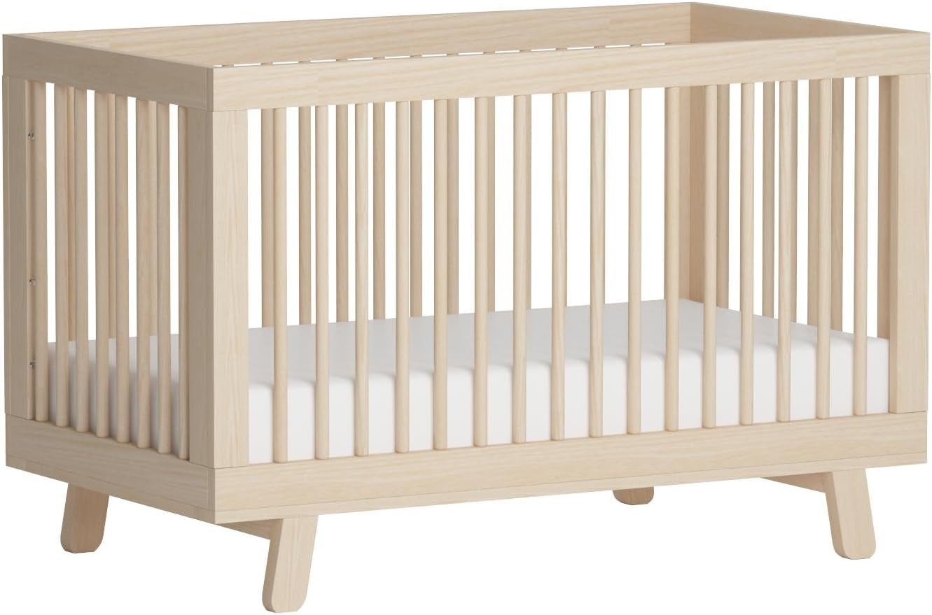 Angled close-up of the light natural wood crib showing slatted sides and tapered legs.