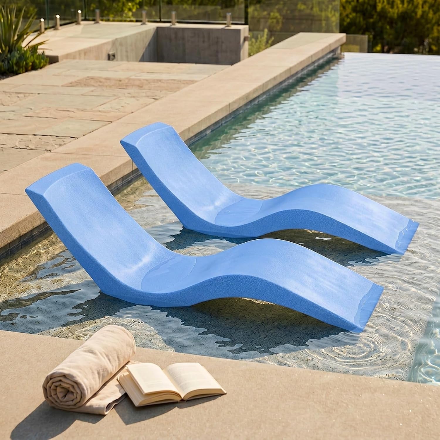 Two light blue loungers placed on a shallow pool sun shelf with a rolled towel and open book nearby.
