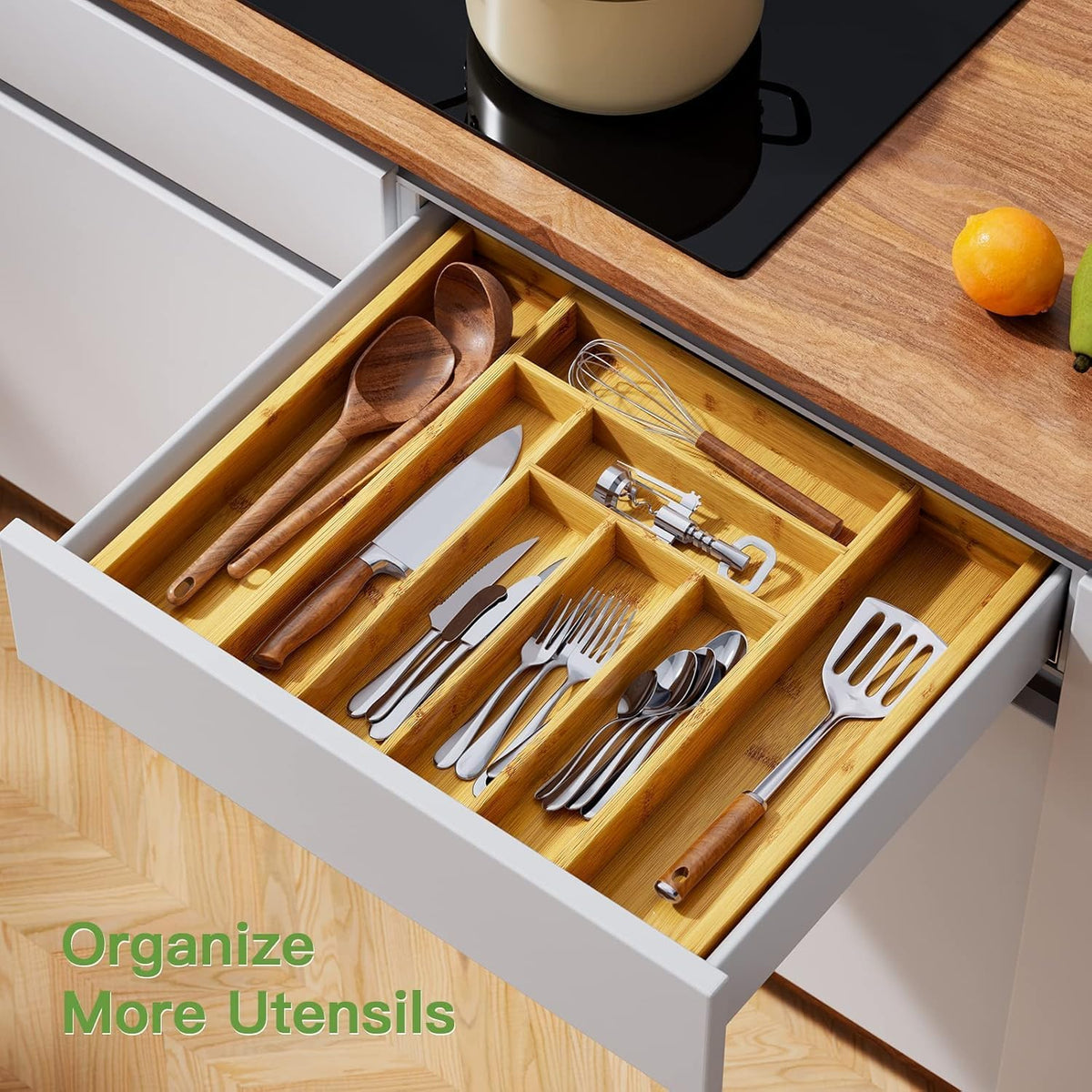 Open drawer with the bamboo organizer filled with forks, spoons, knives and kitchen tools next to a cooktop.