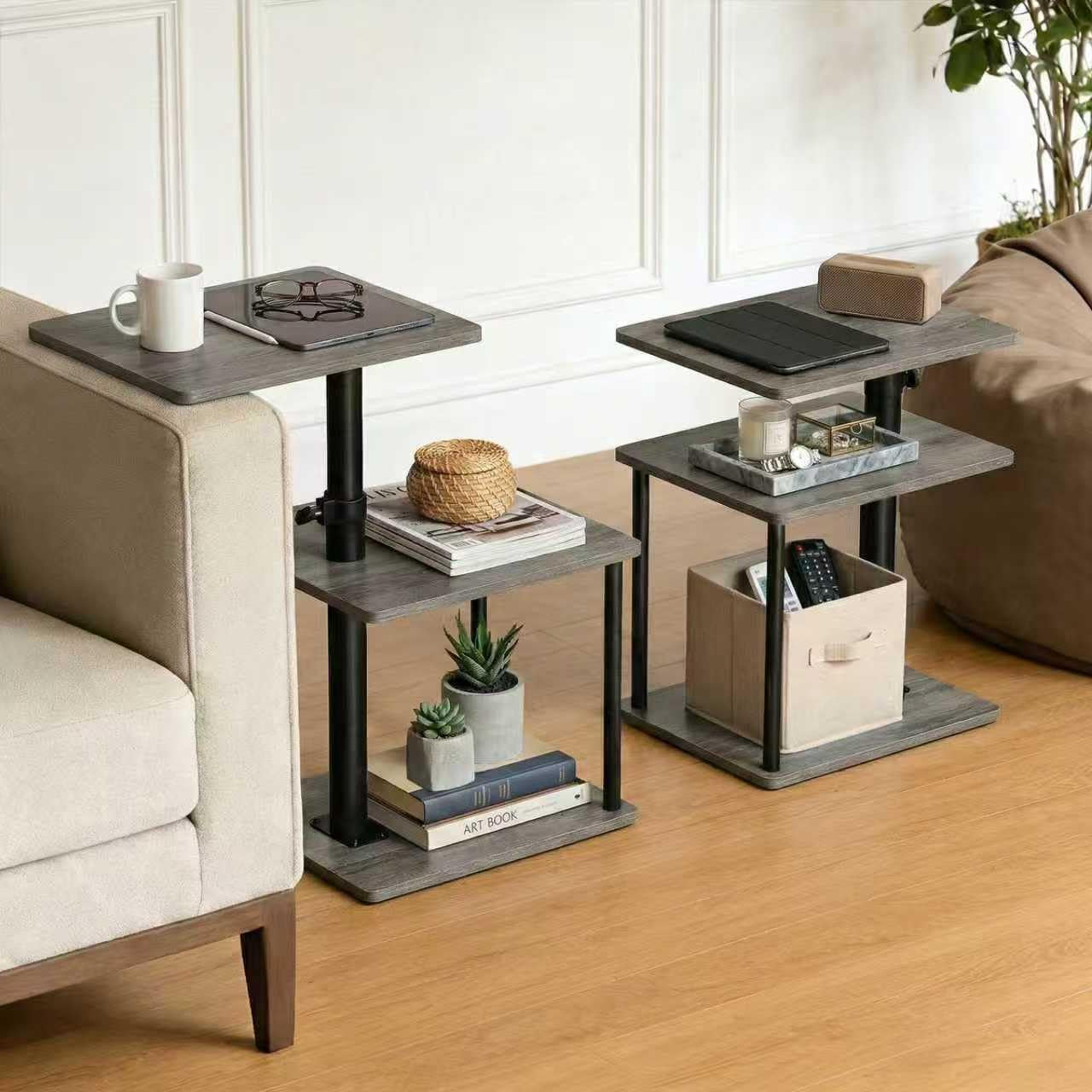Two three-tier C‑shaped side tables in rustic brown beside a sofa and chair, styled with books, plants, a mug and storage