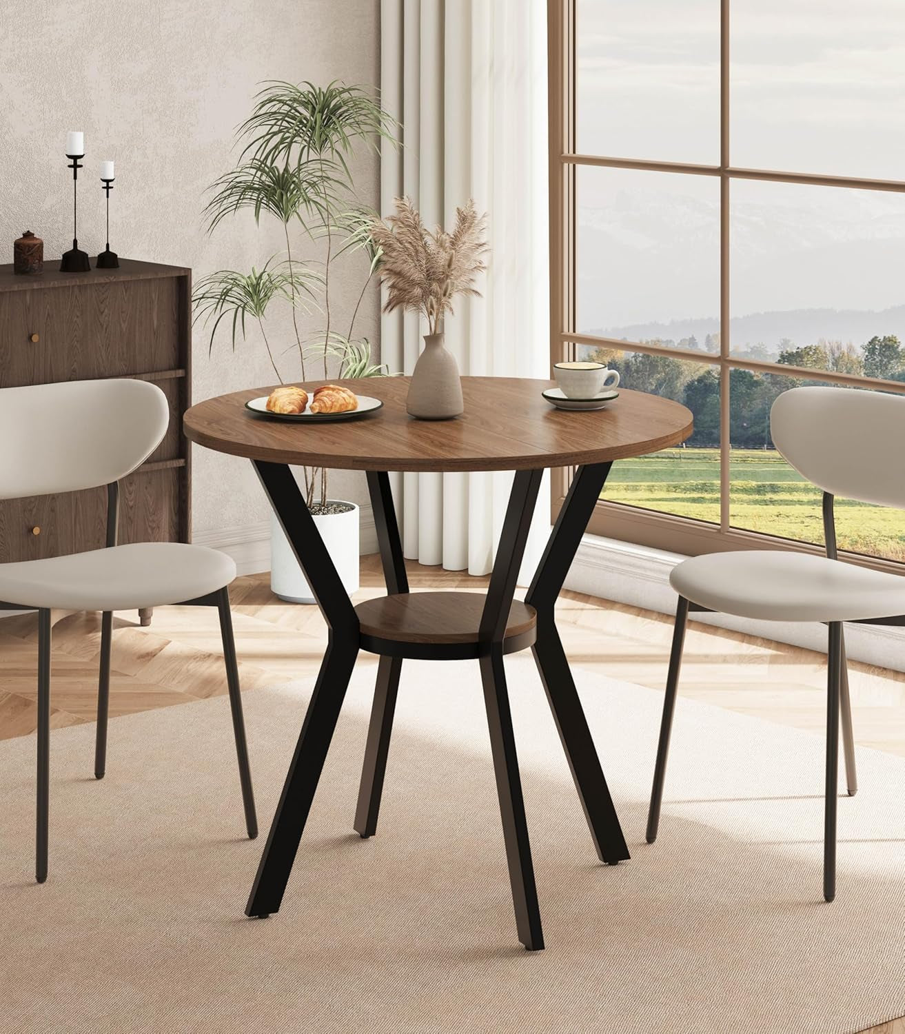 Round wood dining table with black metal base and round storage shelf, staged with plates and vase