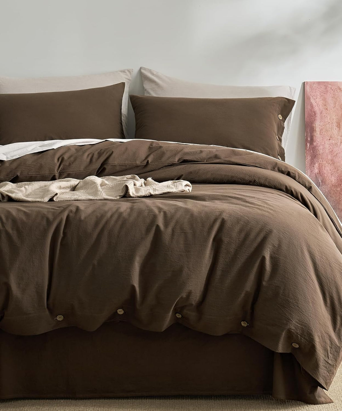 Front view of a bed dressed in chocolate-brown duvet and pillowcases with button closures and a neutral headboard.