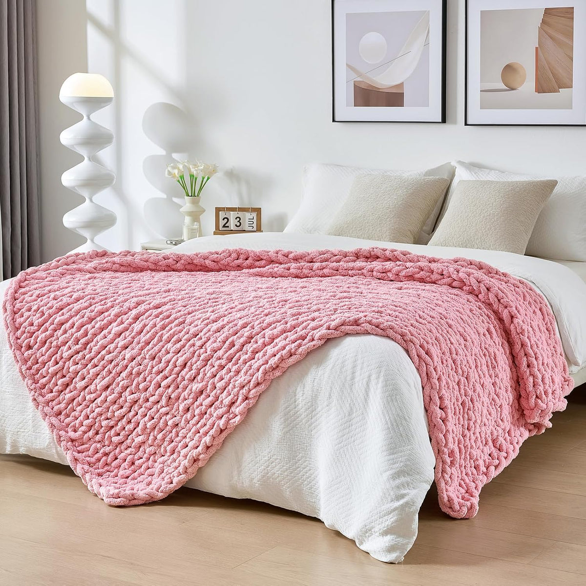 Pink chunky knit throw draped across the foot of a white bed in a bright bedroom.