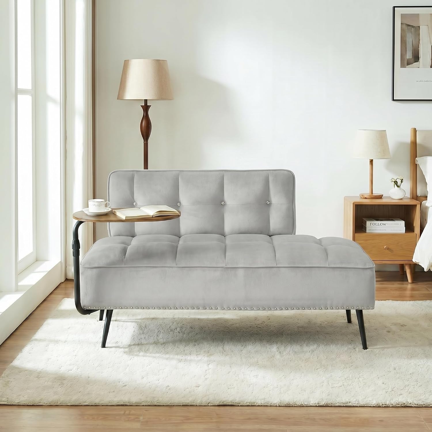 Light gray tufted futon in a bedroom setting with studded trim and black legs.