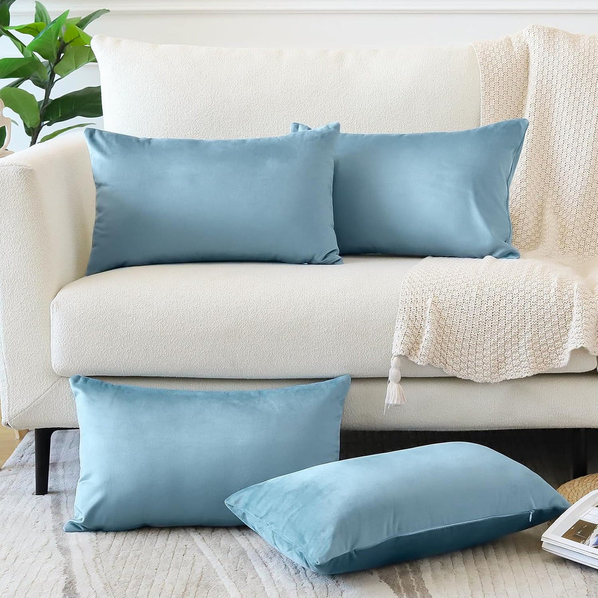 Two light blue rectangular and two matching blue square pillow covers styled on a white sofa.