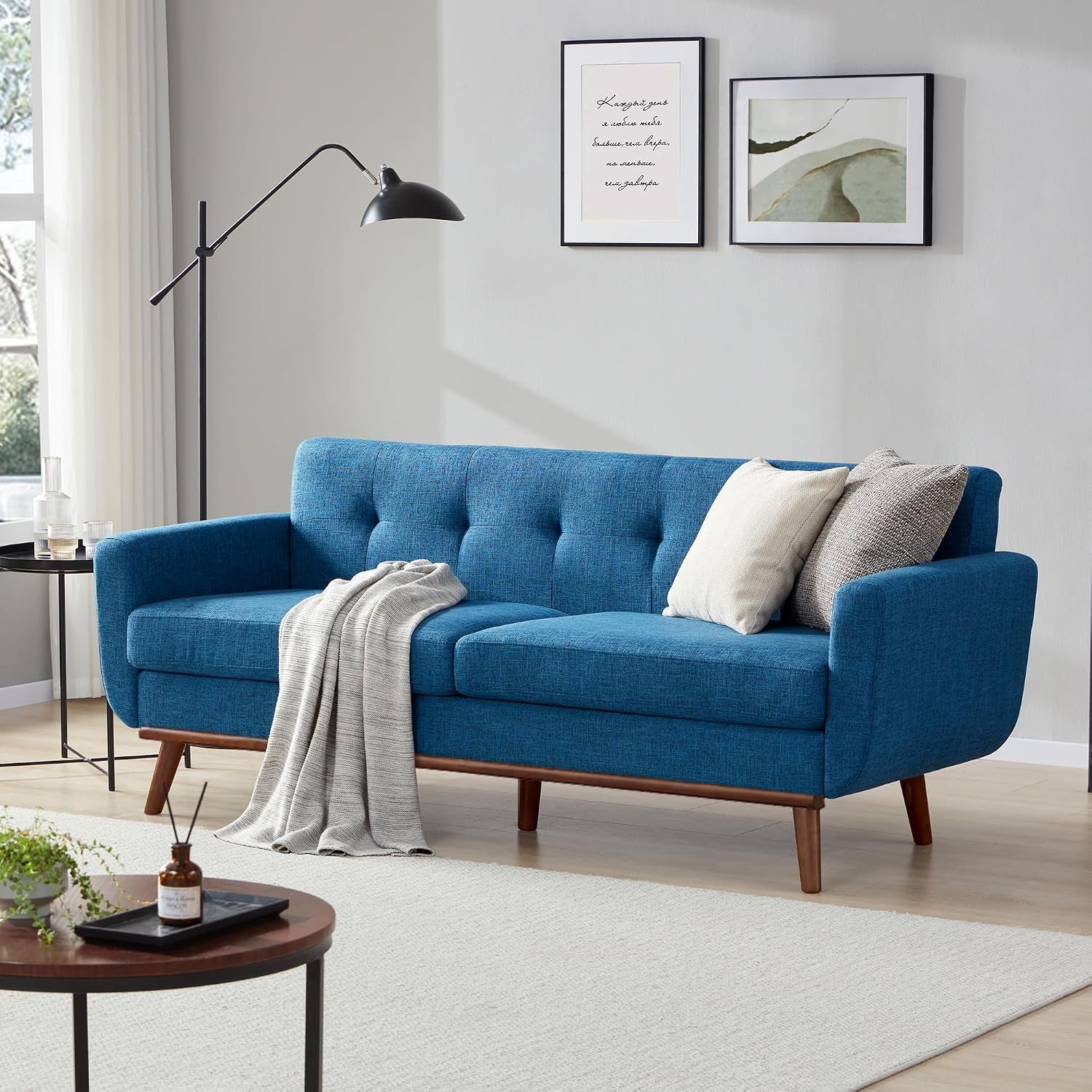 Blue upholstered tufted loveseat with wooden base and two pillows in a styled living room.
