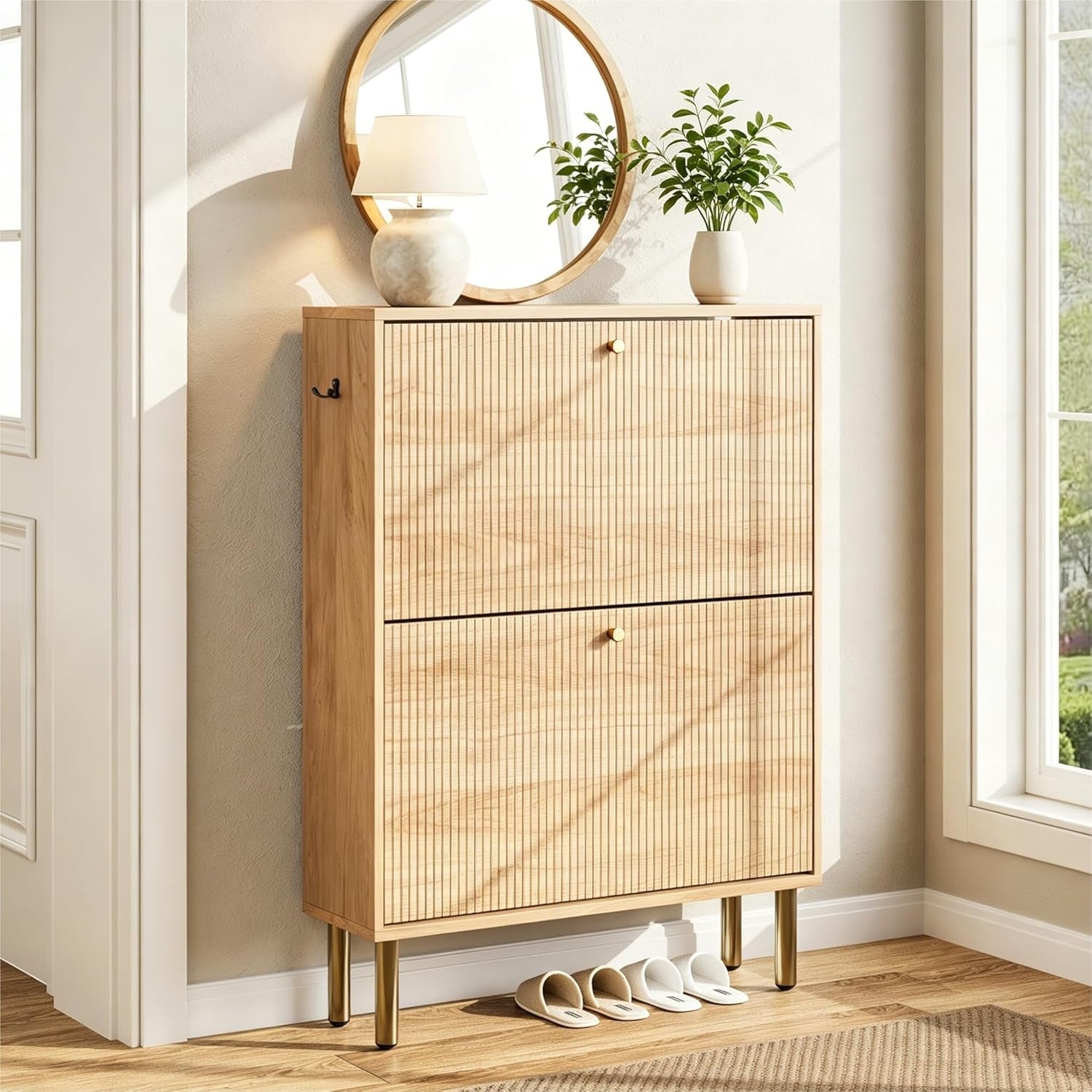 Slim light wood shoe cabinet on brass legs under a round mirror with slippers tucked underneath.