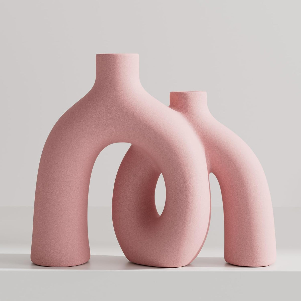 Matte pink textured pair of double-arch donut vases shown on a light shelf