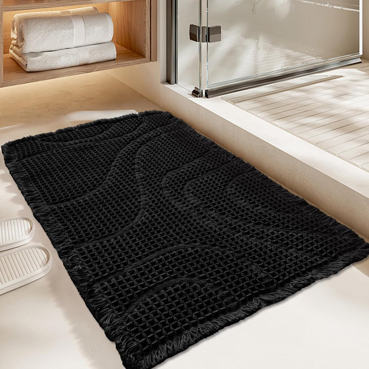 Black wavy-textured rectangular mat with fringe positioned next to a shower entrance.
