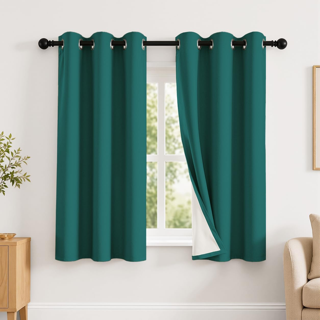 Window dressed with two teal grommet curtains, right panel pulled back to show white thermal backing.