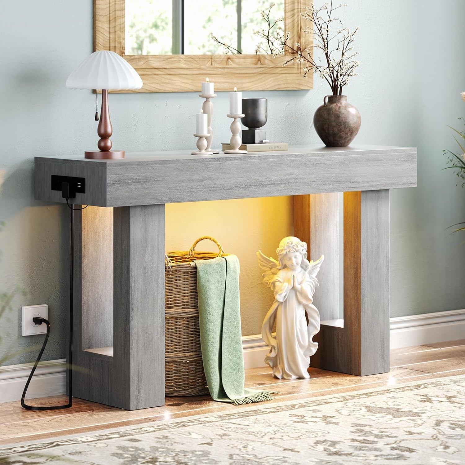 Close crop of a gray console's center showing the glowing interior, basket, draped green throw and angel statue beside it.