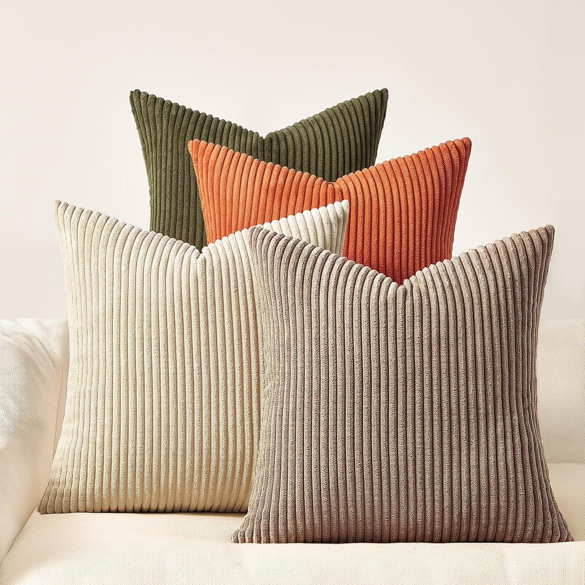 Five ribbed square pillows in olive green, burnt orange, cream and taupe on a light sofa