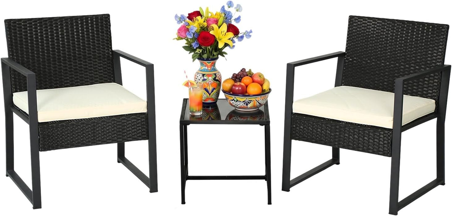 Two dark rattan armchairs with cream seat cushions flanking a small glass-top side table with fruit and flowers