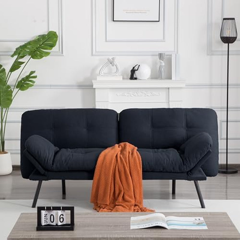 Black futon sofa with angled armrests, an orange throw draped over the seat, and minimalist décor behind it.